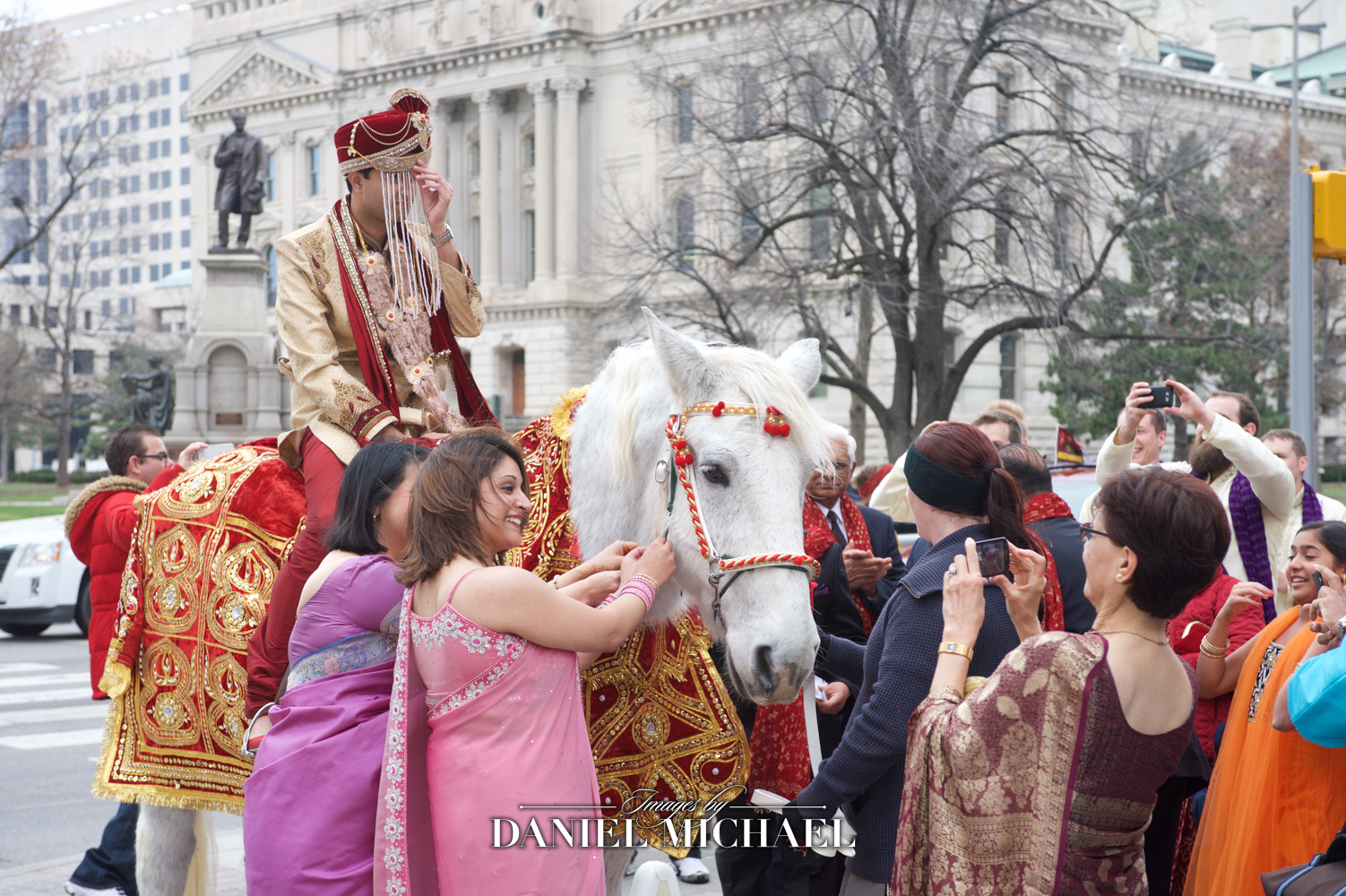 Indian groom in traditional attire riding a white horse during baraat ceremony
